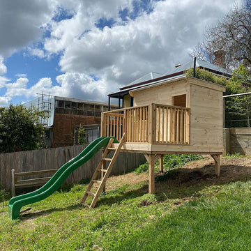 A raised platform with cubby house and slide on a sloped grassy area