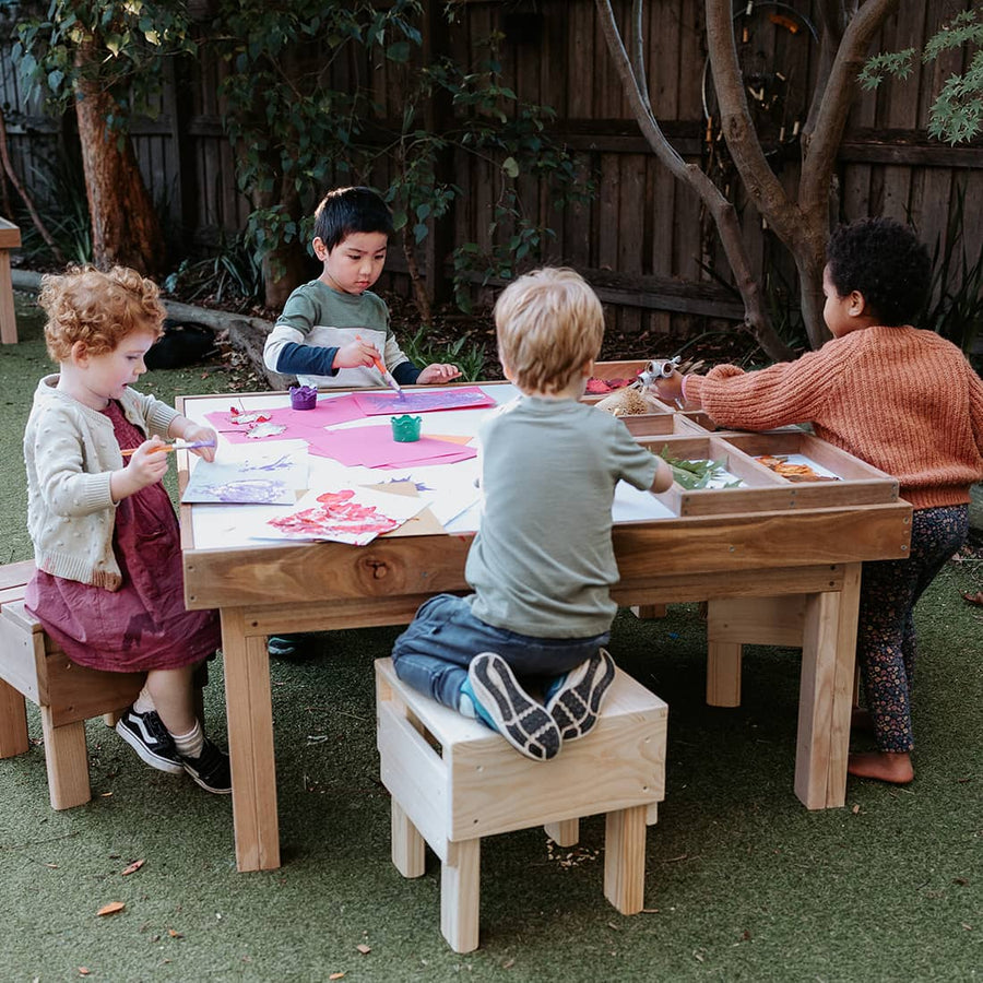 Kids sitting  and crafting at a hardwood outdoor table in an educational play area