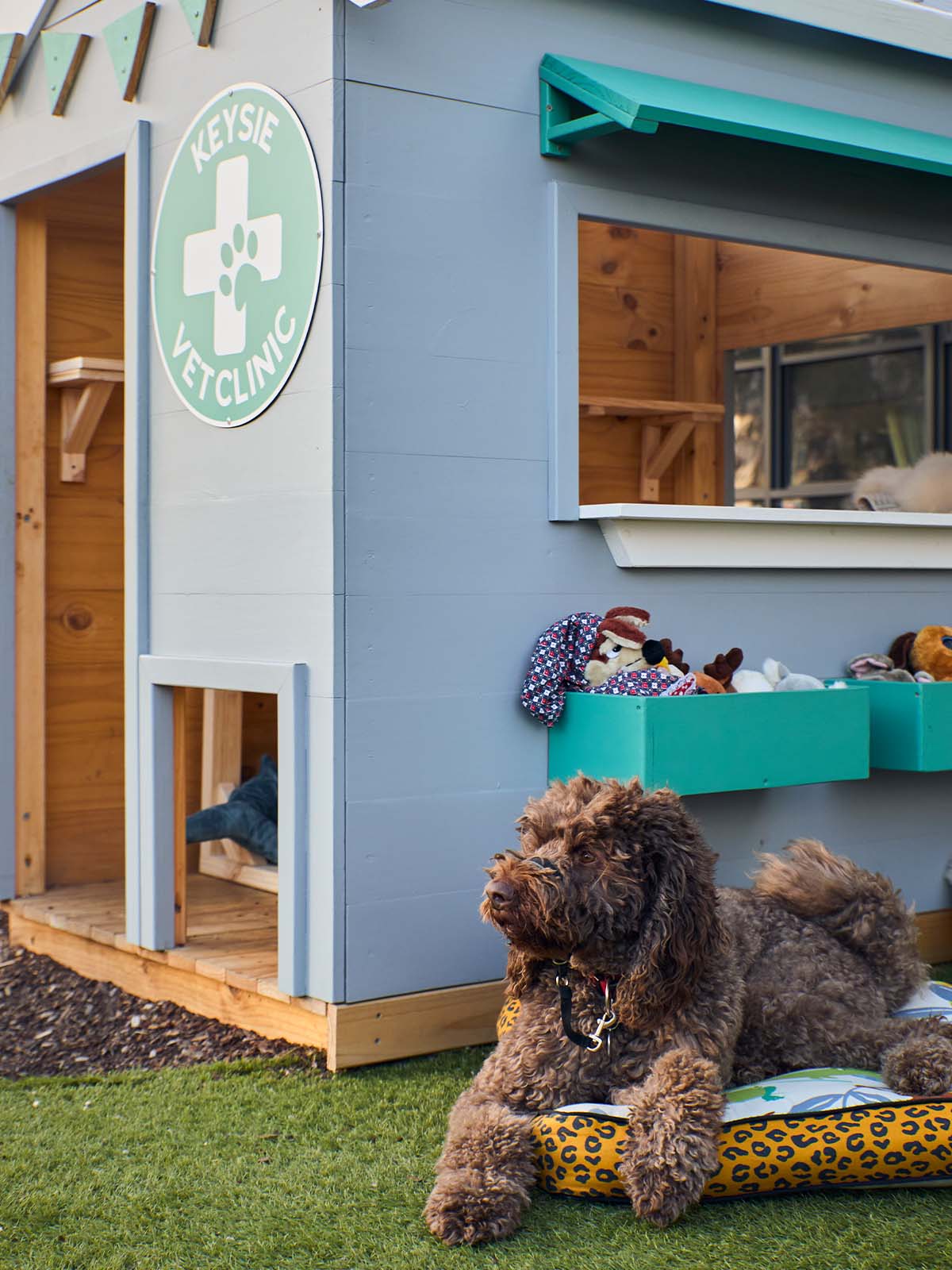 Close up of a vet themed grey and green cubby house front corner staged with soft toys and cut dog posing out the front