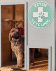 Close up of a vet themed grey and green cubby house doorway and matching doggy door with a cute dog posing in the doorway