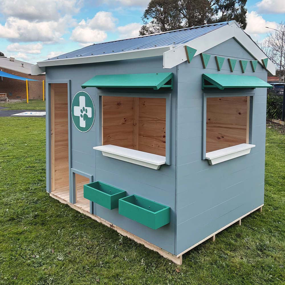 A vet themed grey and green cubby house on grass in a school yard close up 