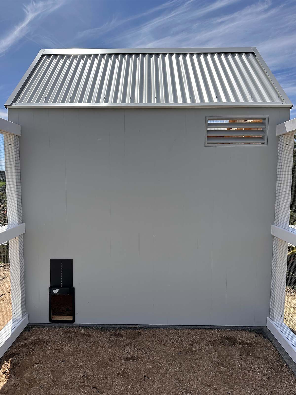 Side wall of a grey barn style chicken coop with vent and automated chicken door