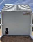 Side wall of a grey barn style chicken coop with vent and automated chicken door