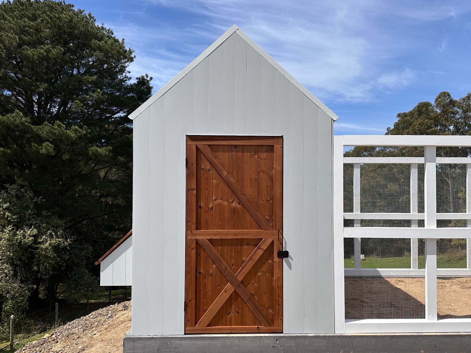 Close up of a thermory timber door on a large grey barn style chicken coop on a sunny day