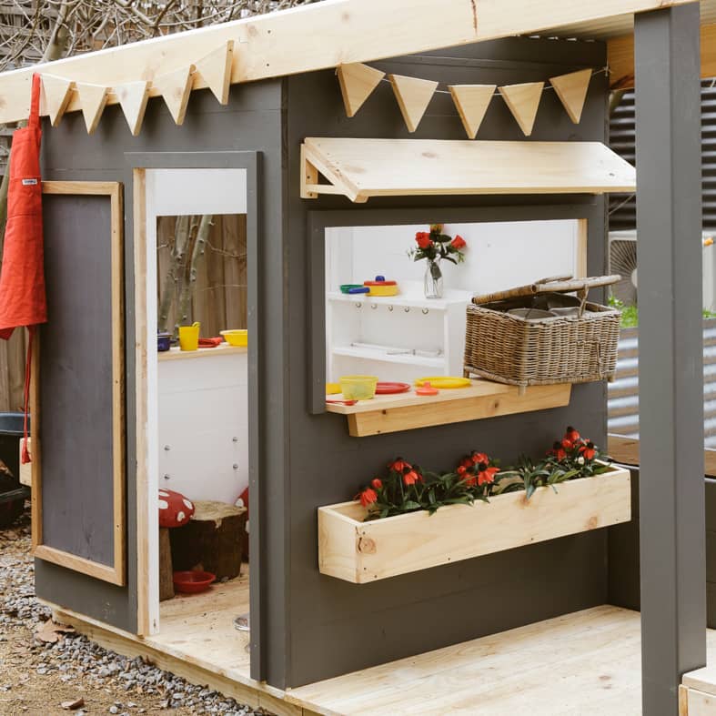 A wooden cubby house with front verandah styled with toys and painted charcoal and white