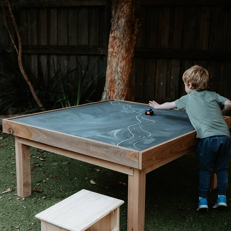 A boy drawing on a chalkboard table in an early learning centre yard