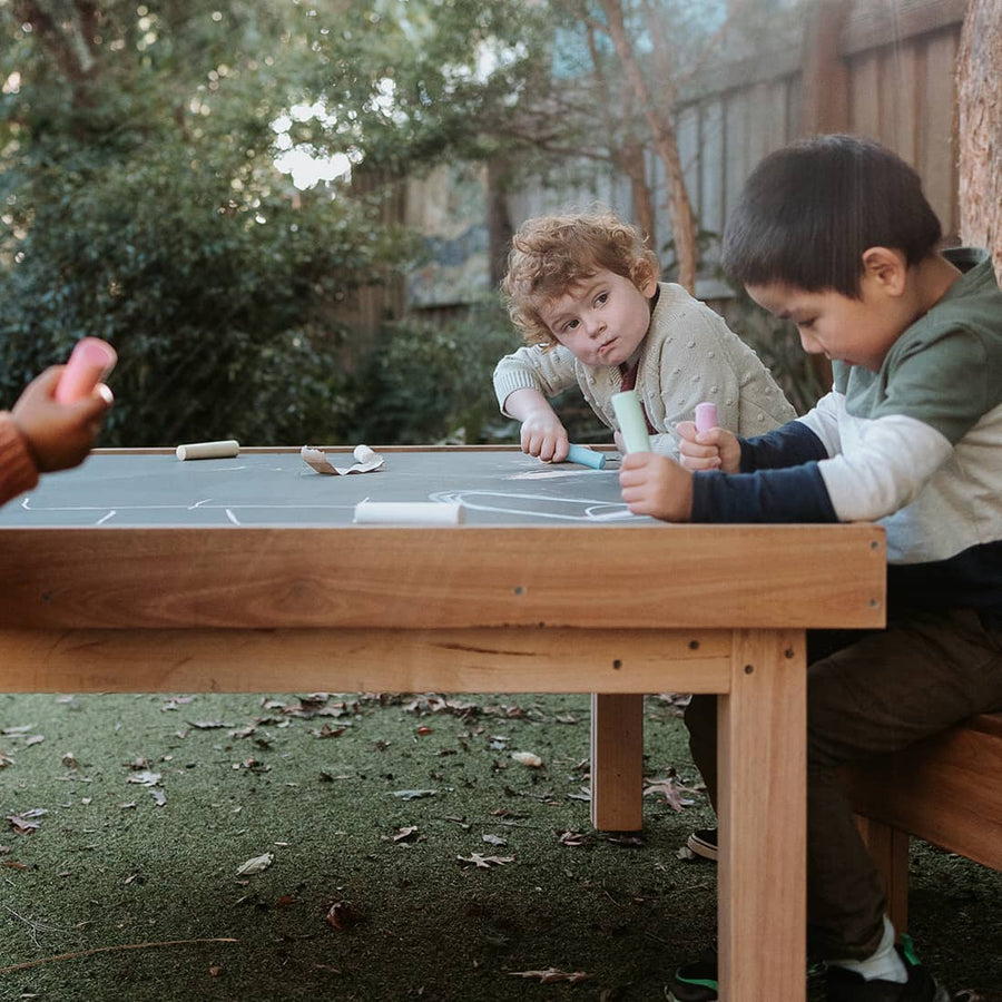 Kids gathered around drawing on an outdoor chalkboard table