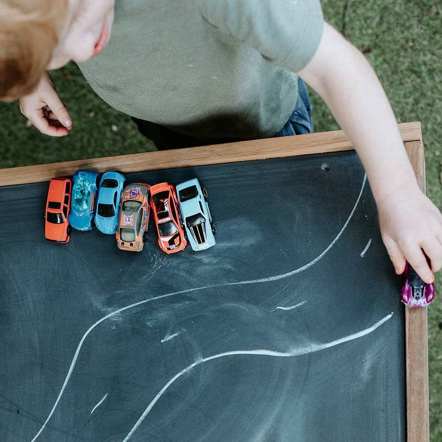 A boy plays with toy cars on a chalkboard table with drawn road map