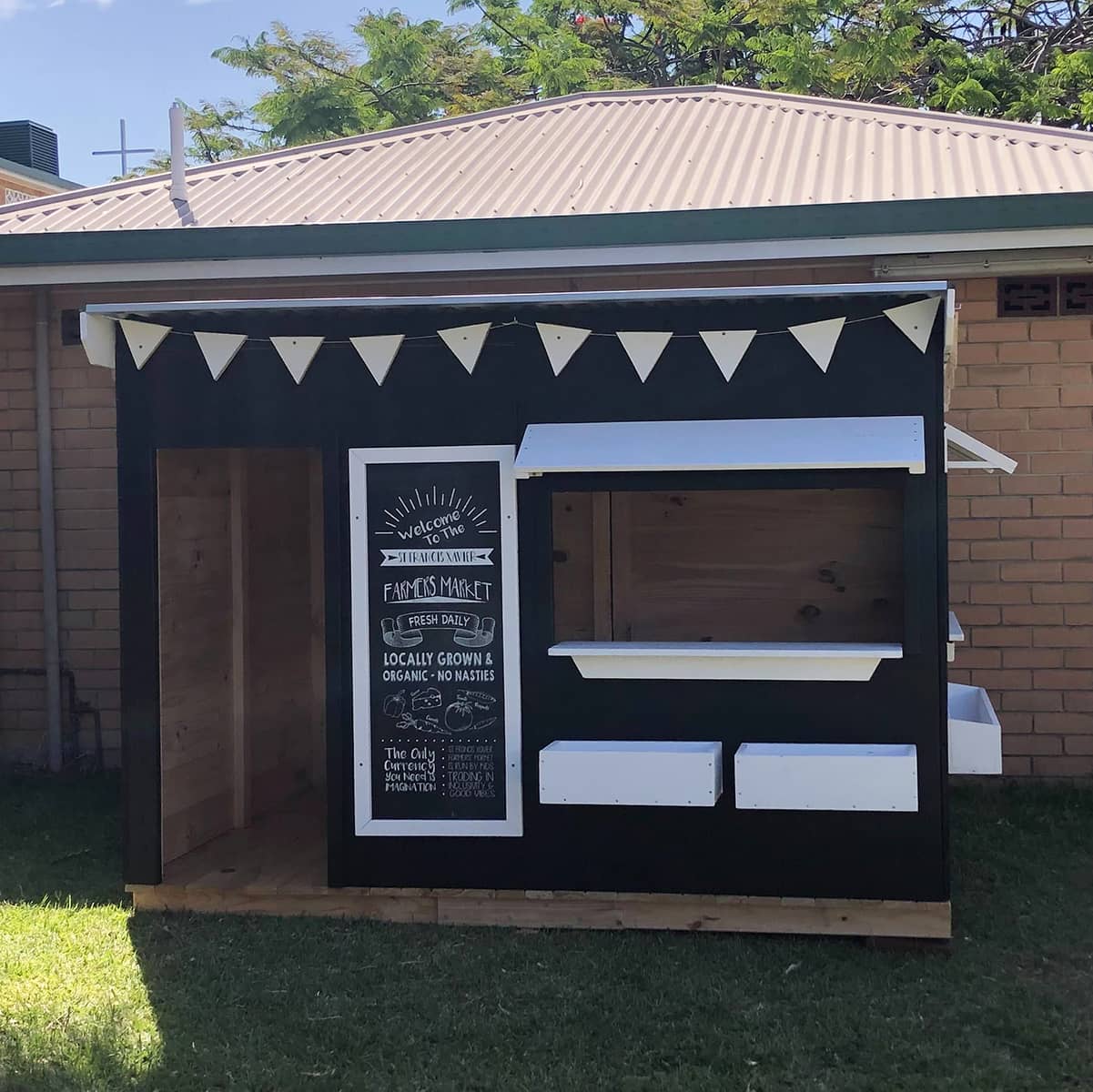 A painted farmers market themed wooden cubby house in an education setting