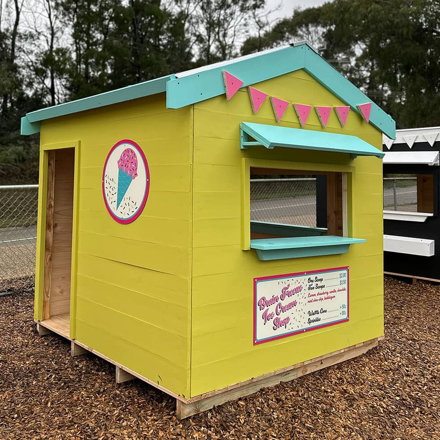 A painted wooden cubby house themed as an ice cream shop as part of an education village play space
