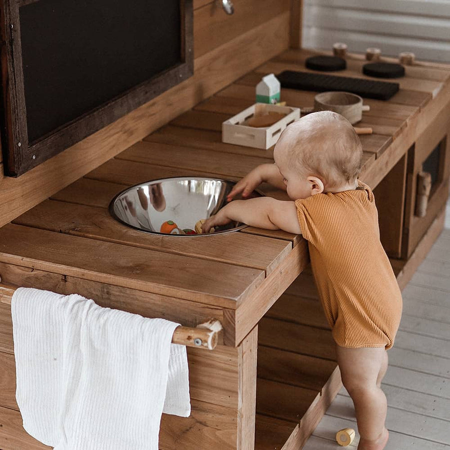 A baby plays at a wooden outdoor mud kitchen