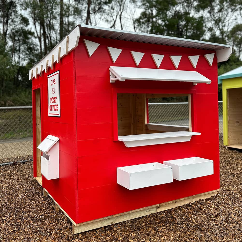 A red and white painted wooden cubby house styled as a post office in an education village play space