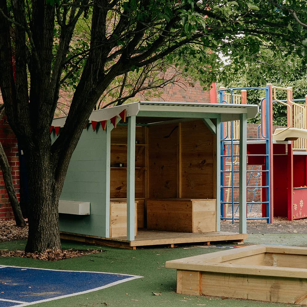 An aqua painted potting shed in front of a garden bed in a school playground