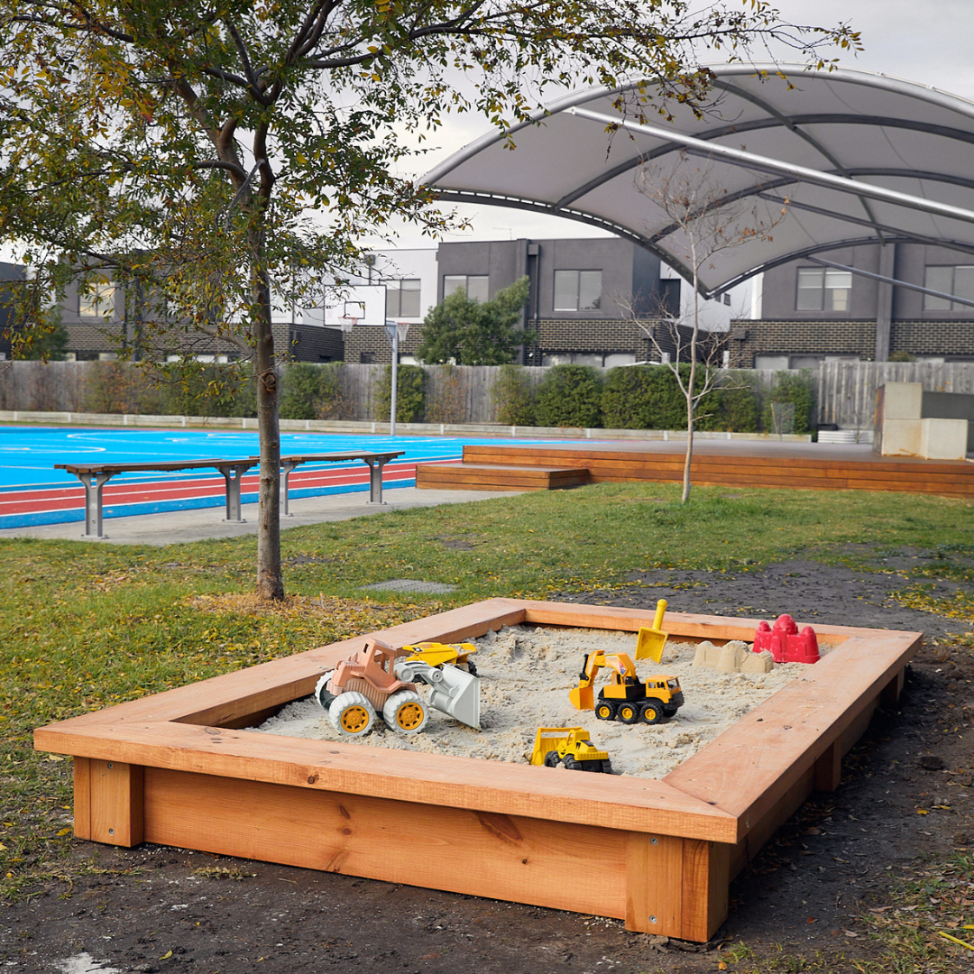 Raised timber sandpit in school grounds with toys and timber deck in background