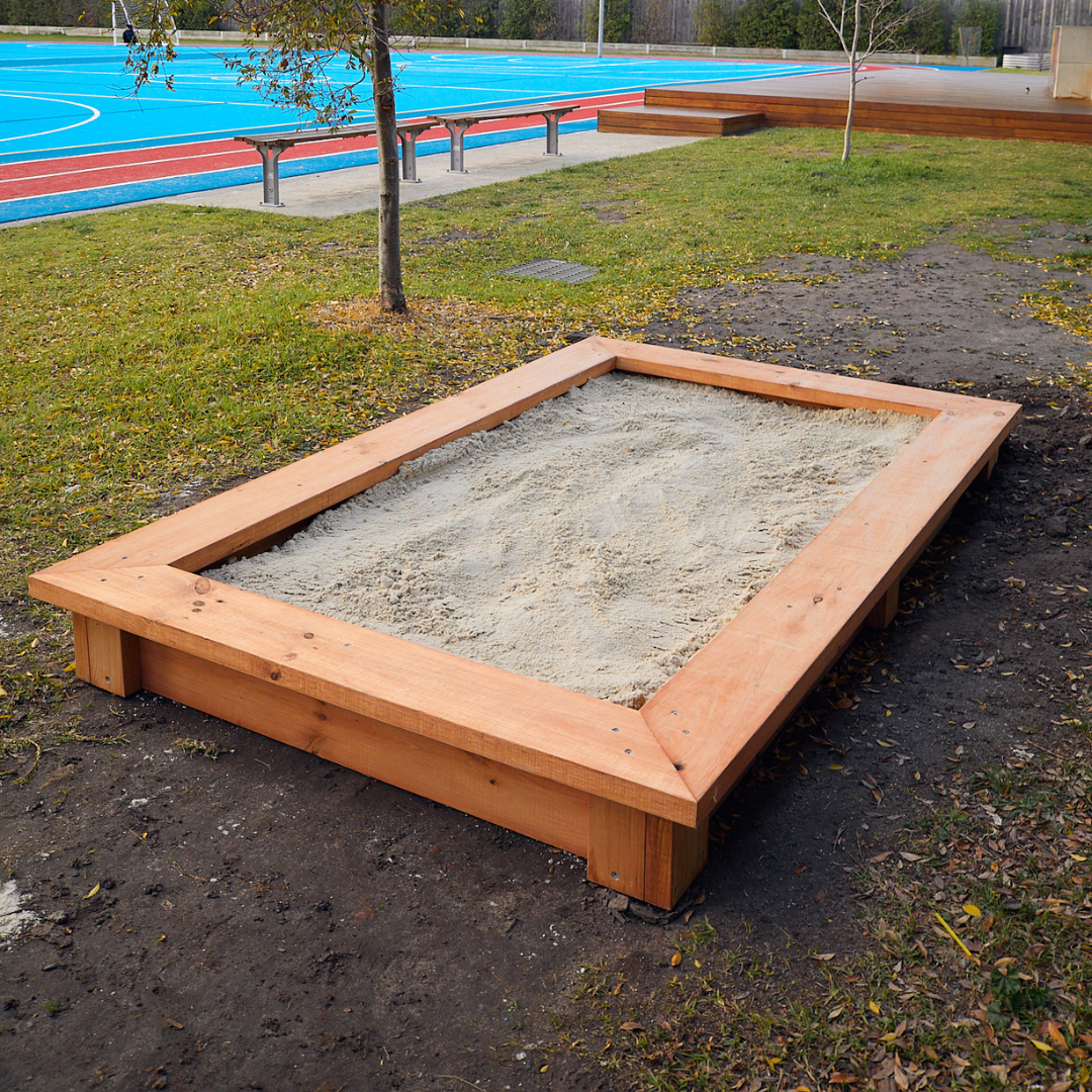 Raised timber sandpit in school grounds with blue playing fields in the background