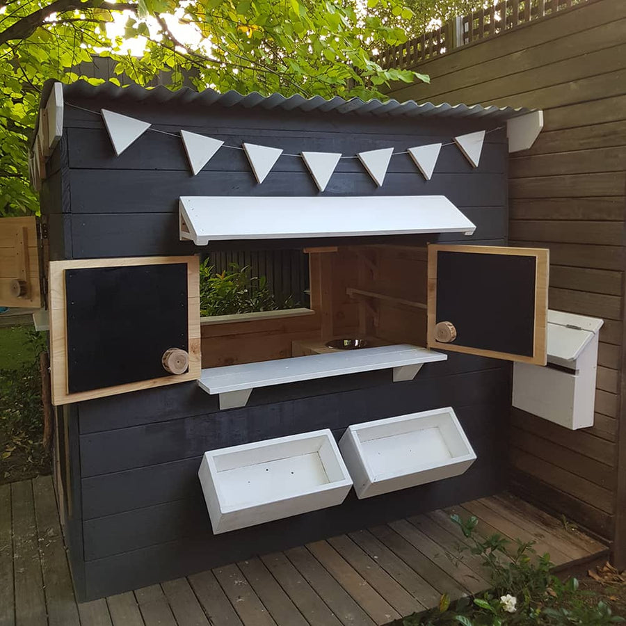 A close up view of the front of a painted timber cubby house with open windows and accessories