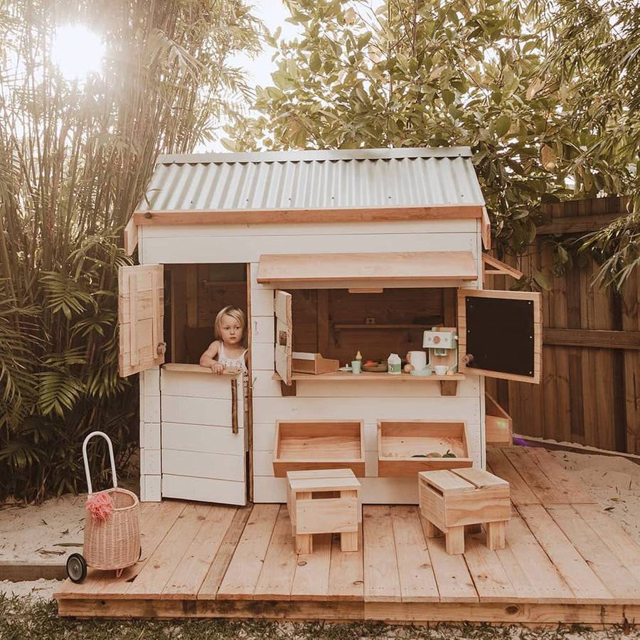 A child plays inside a beautiful white painted wooden pitched roof cubby house with accessories and toys