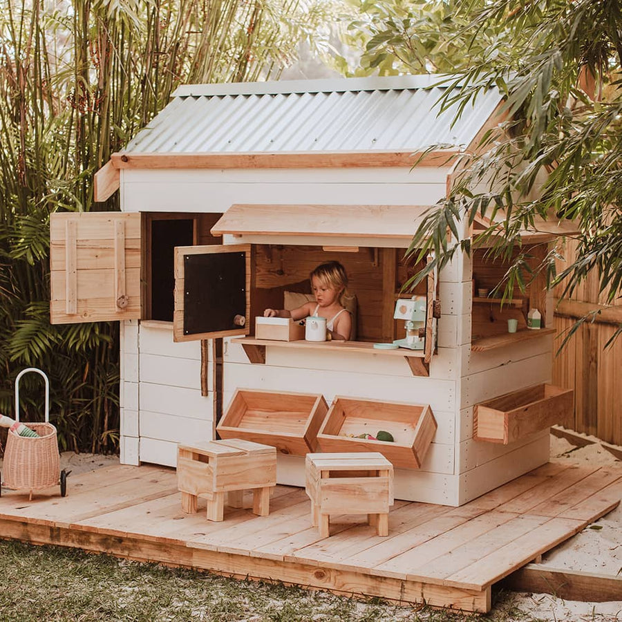 A child plays inside a beautiful white and timber pitched roof cubby house