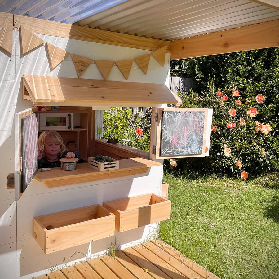 A child playing at the window of a wooden cubby house