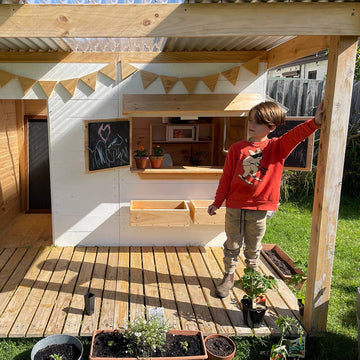 A boy relaxes in a painted wooden cubby house with verandah roof