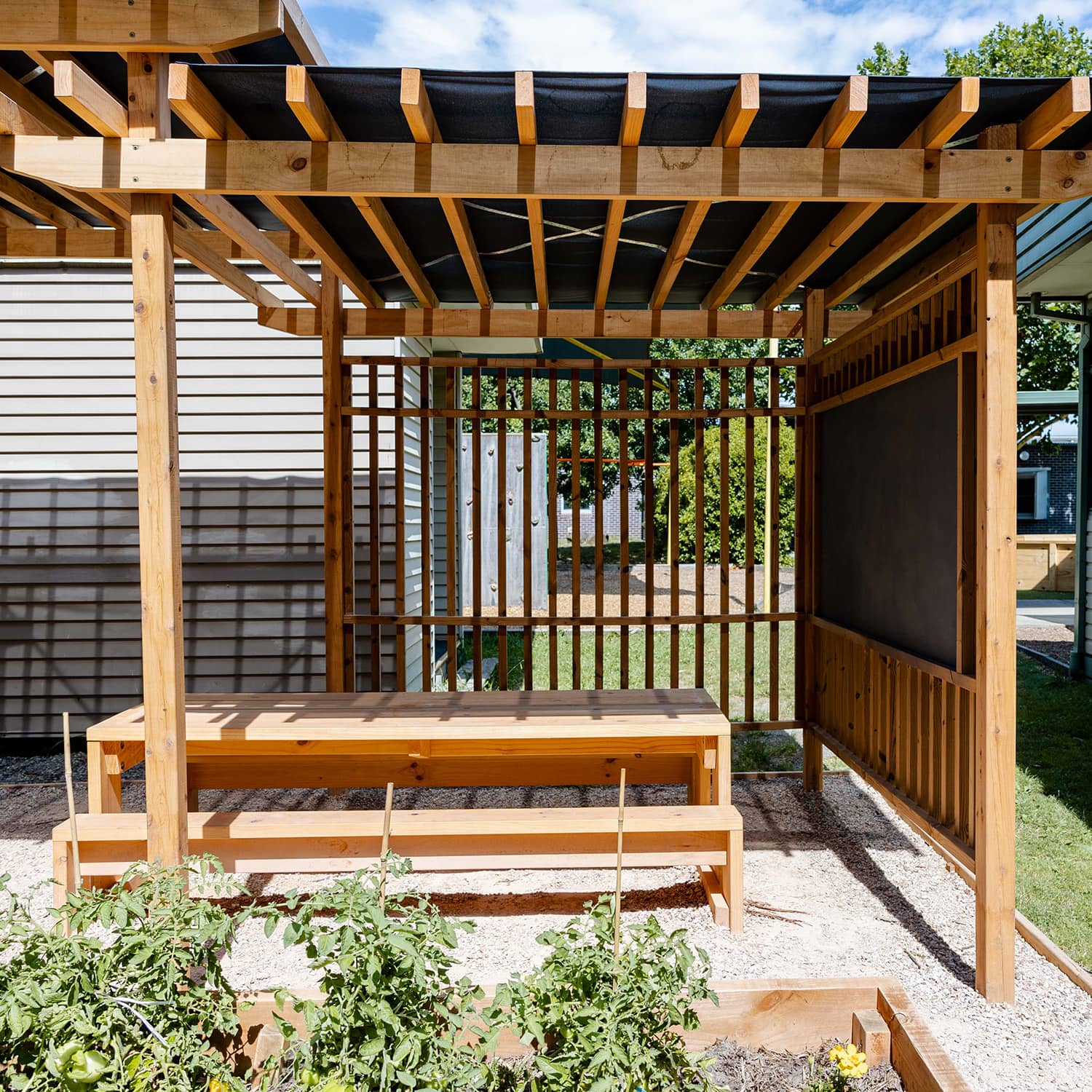 Timber outdoor pergola with benches and tables in bright sun