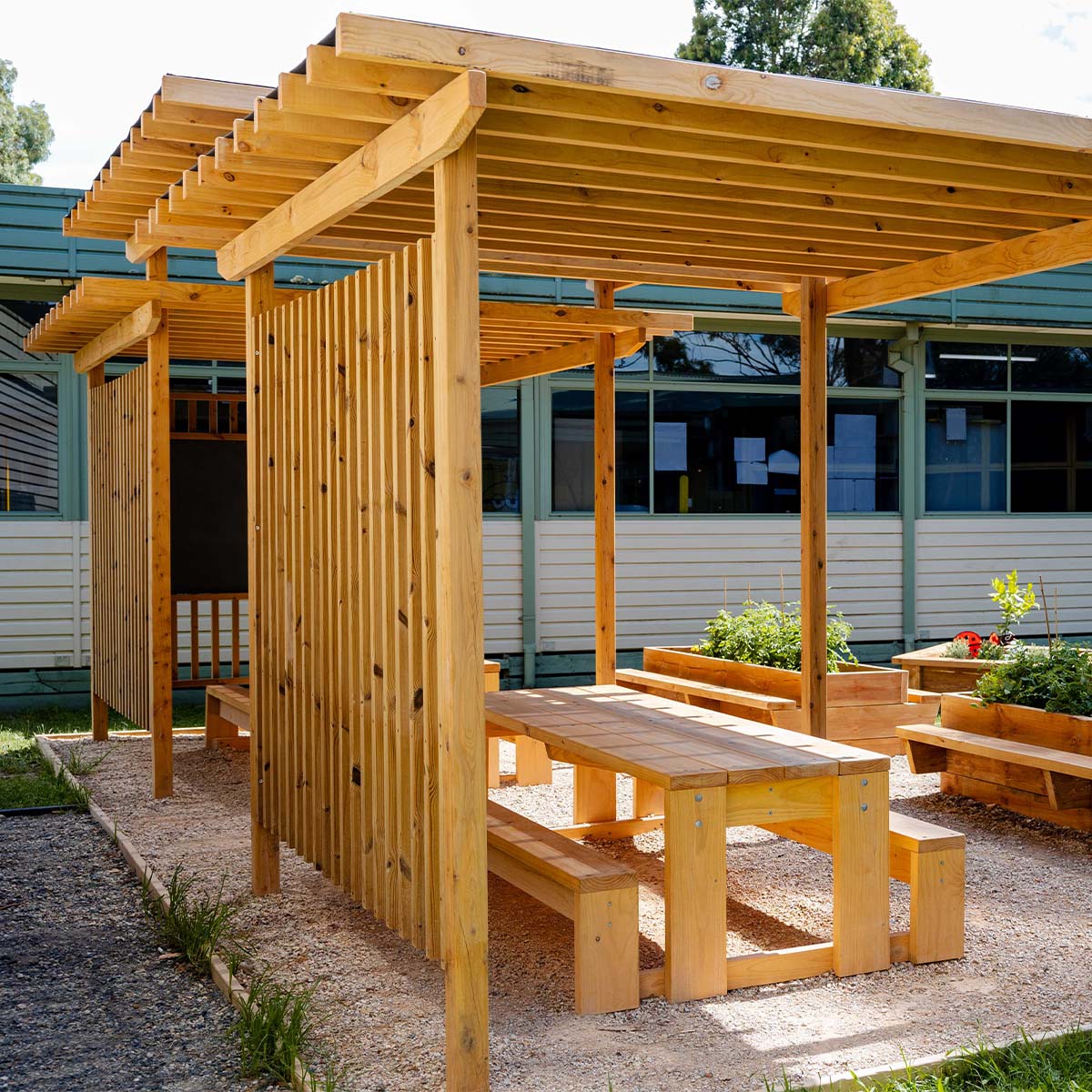 Timber picnic table with benches under a Timber pergola in an outdoor setting.