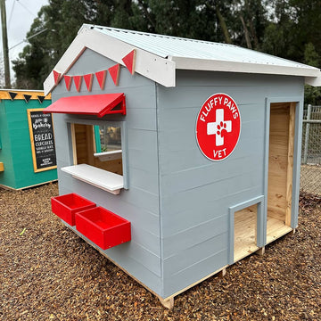 A grey painted wooden cubby house with red and white trims in a school play ground