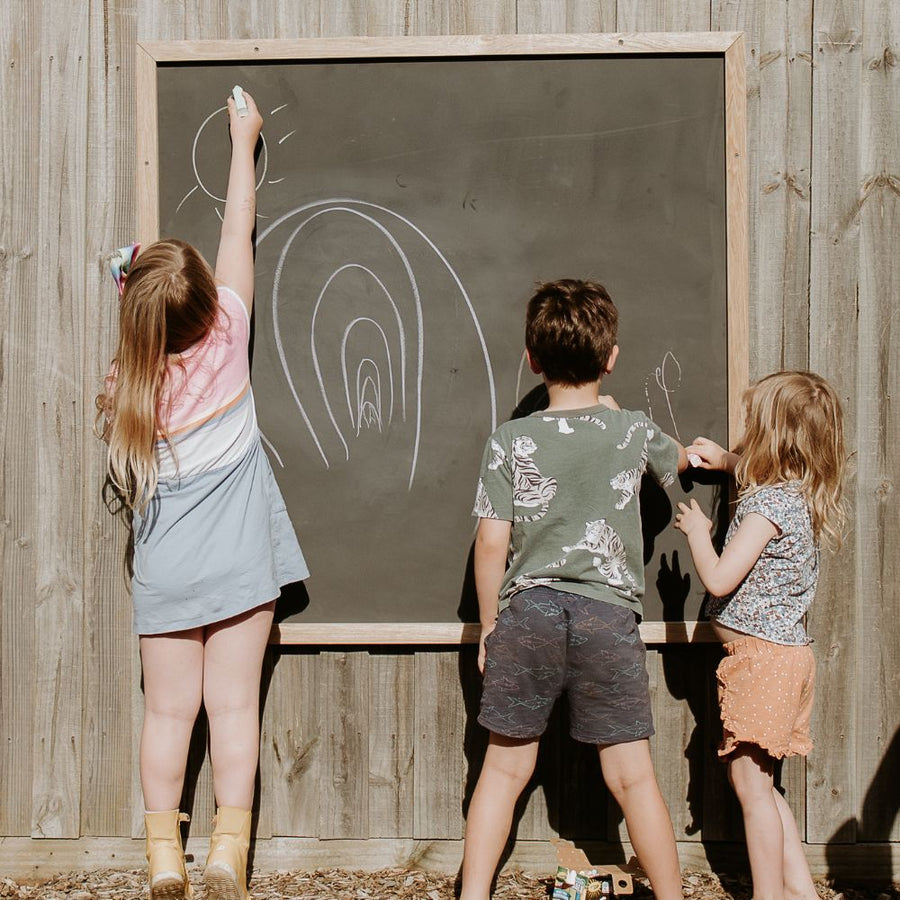 kids drawing in chalk on their outdoor framed fence blackboard