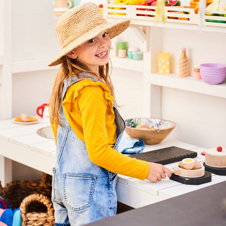 A girl plays at her colourful cubby house kitchen bench