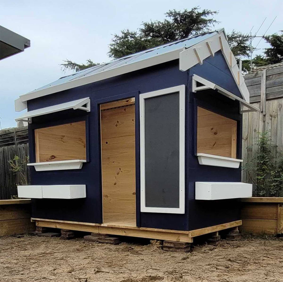A painted wooden cubby house with a pitched roof and accessories in an education setting