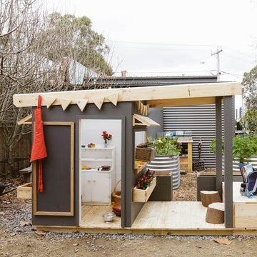 A painted wooden cubby house with front verandah in a childcare education outdoor space.