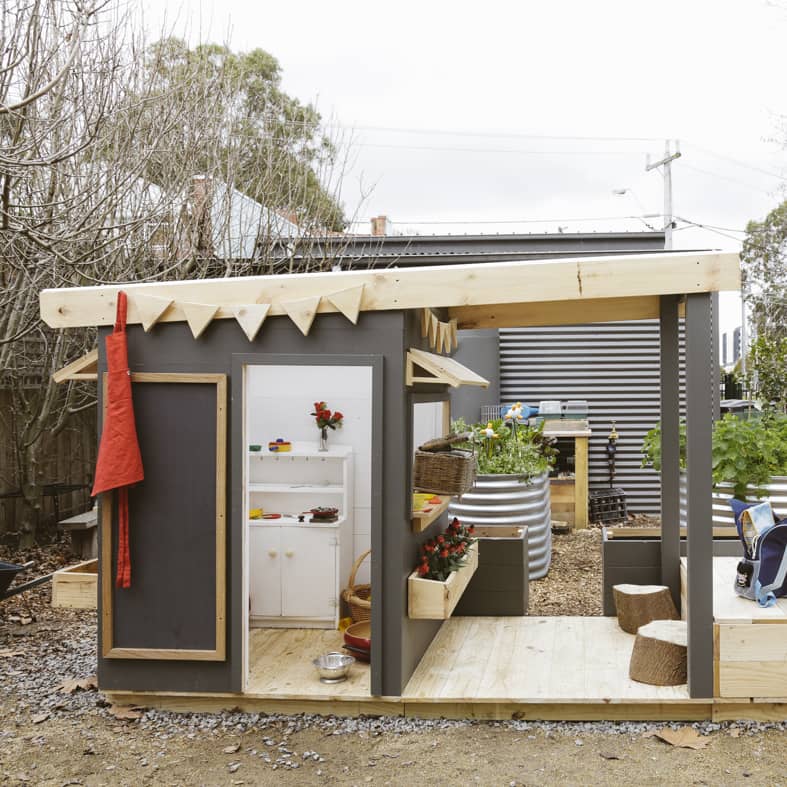 A painted wooden cubby house with front verandah in a childcare education outdoor space.