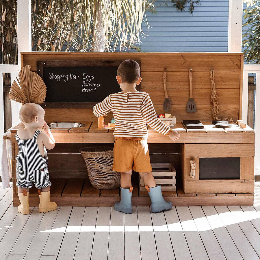 A baby and preschooler play at a wooden play kitchen with oven