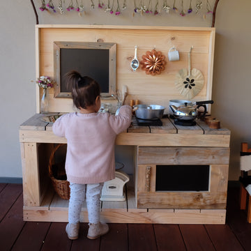 Little girl role playing at a wooden kids play kitchen bench