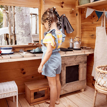 A girl plays at her cubby house kitchen bench